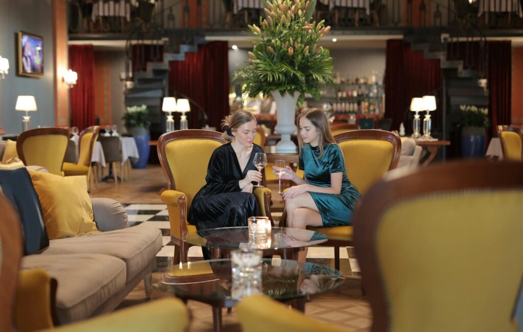 Two women engage in conversation over drinks in a stylish hotel lounge, featuring elegant decor and cozy seating.